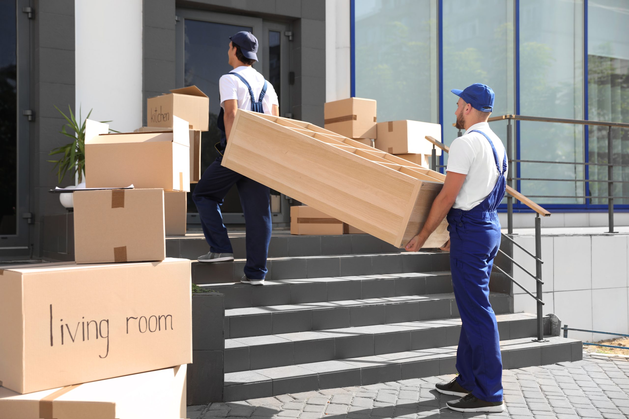 Umzugshelfer tragen Möbel und Kartons ins Haus